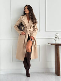 Woman wearing a beige coat and brown knee-high boots in a minimalistic room.