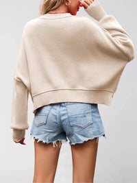 Person wearing a beige sweater and denim shorts on a plain background