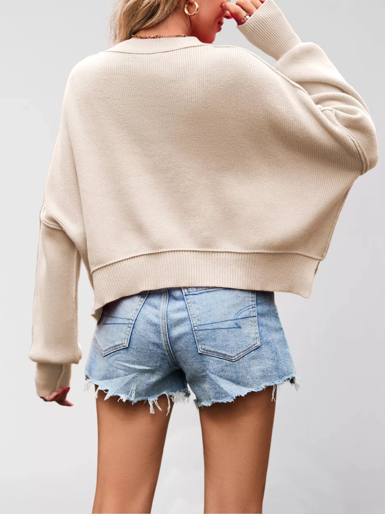 Person wearing a beige sweater and denim shorts on a plain background