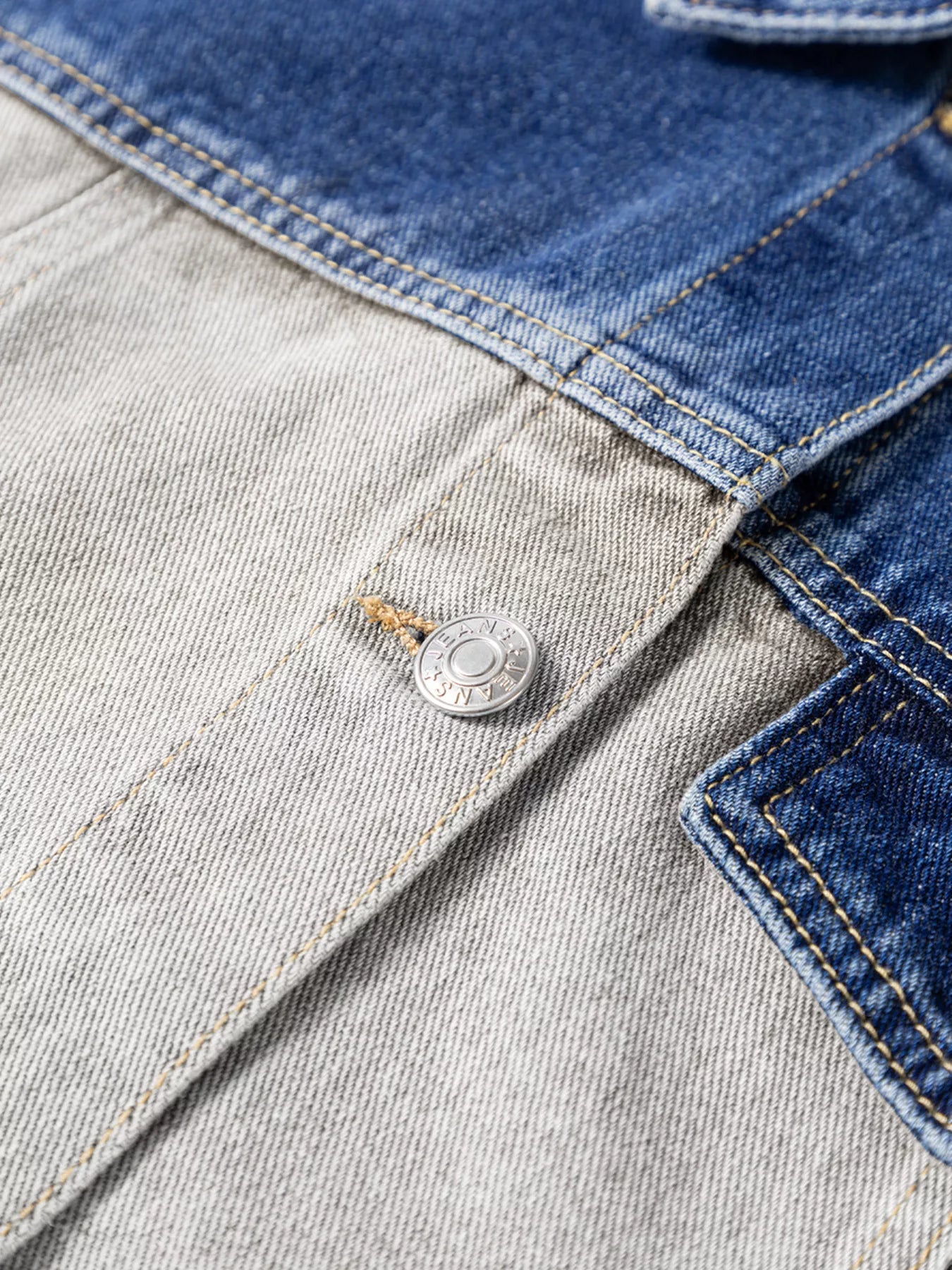 Close-up of a denim jacket with a button detail on a light gray background