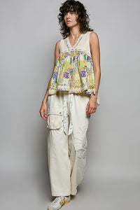 Woman wearing a colorful sleeveless top and white pants against a gray background