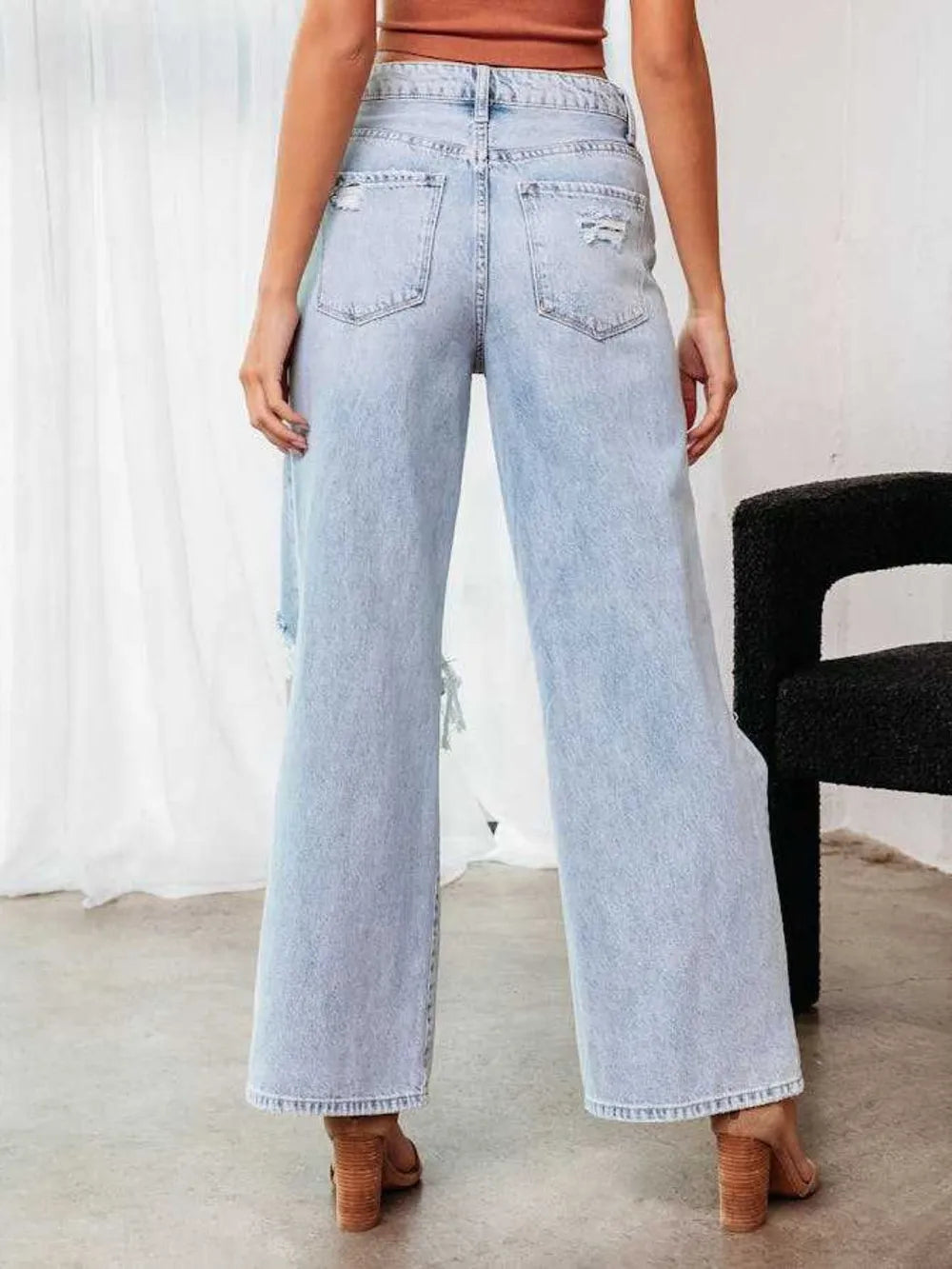 Light blue jeans worn by a person with a white curtain and black chair in the background