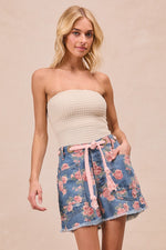 Woman wearing a strapless top and floral denim skirt on a beige background