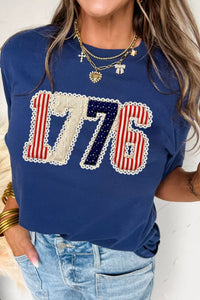 Person wearing a blue t-shirt with '1776' design, standing against a neutral background