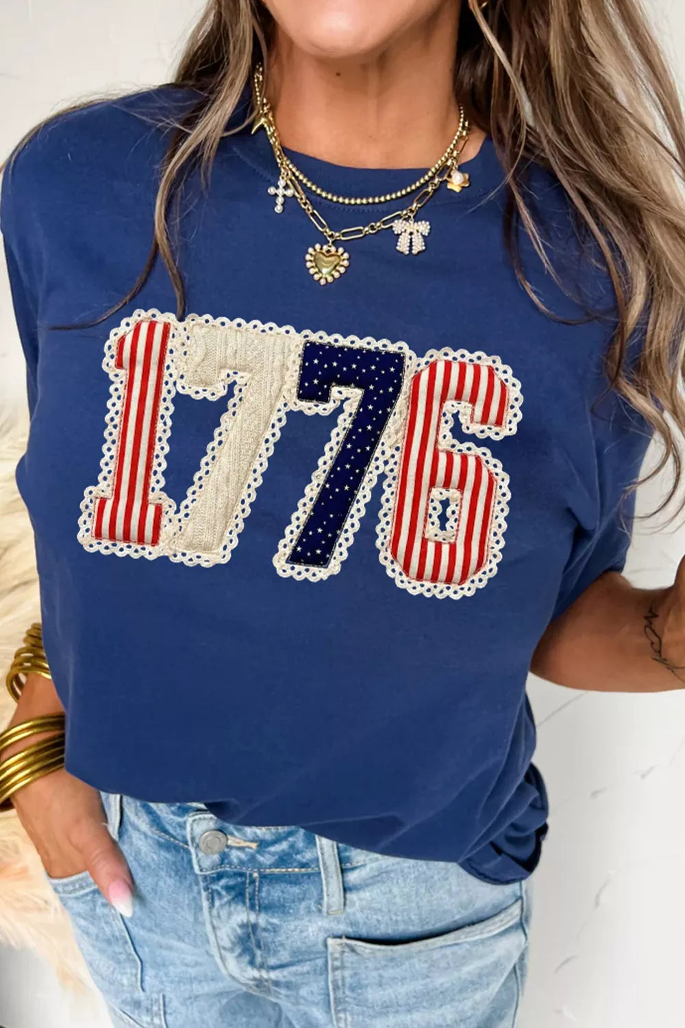 Person wearing a blue t-shirt with '1776' design, standing against a neutral background