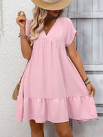 Woman wearing a pink dress with a straw hat against a wooden wall.