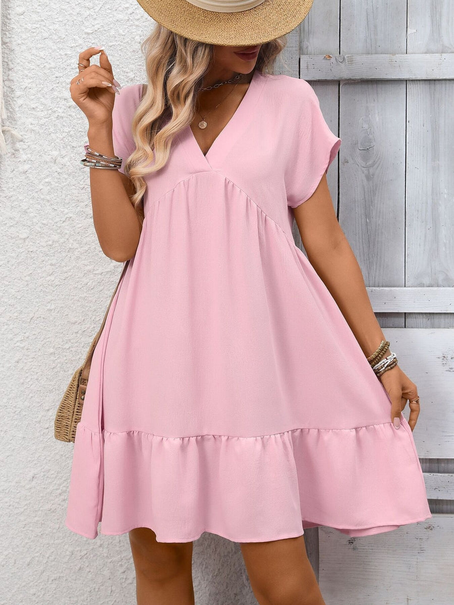 Woman wearing a pink dress with a straw hat against a wooden wall.
