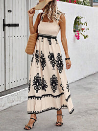 Woman wearing a beige dress with black patterns, standing in front of a white wall.