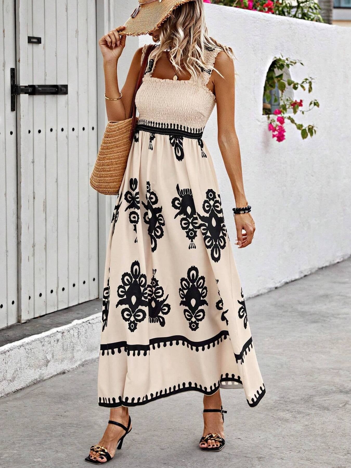 Woman wearing a beige dress with black patterns, standing in front of a white wall.