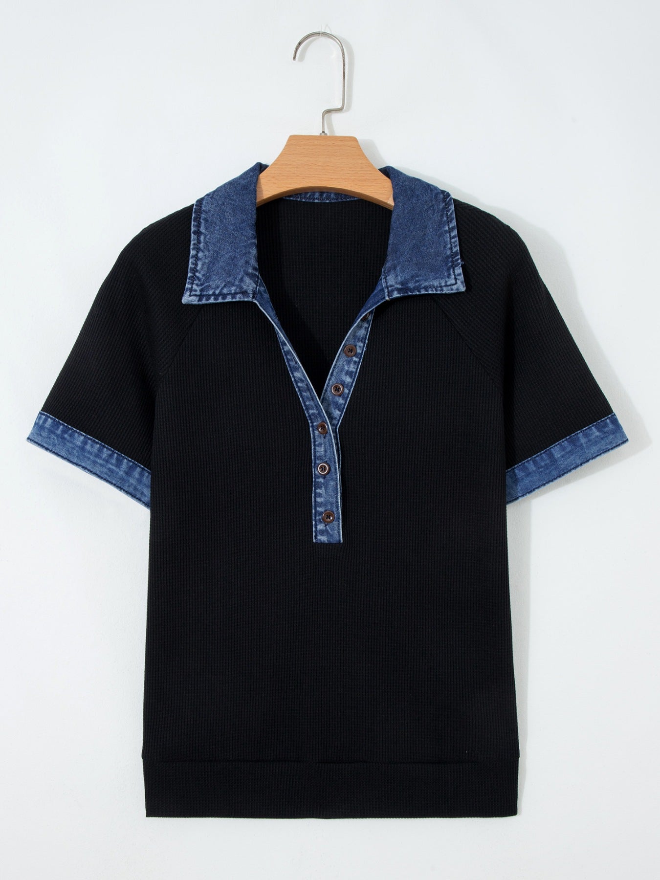 Black t-shirt with denim collar and cuffs on a wooden hanger against a white background