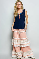 Woman wearing a navy sleeveless top and pink lace pants on a gray background