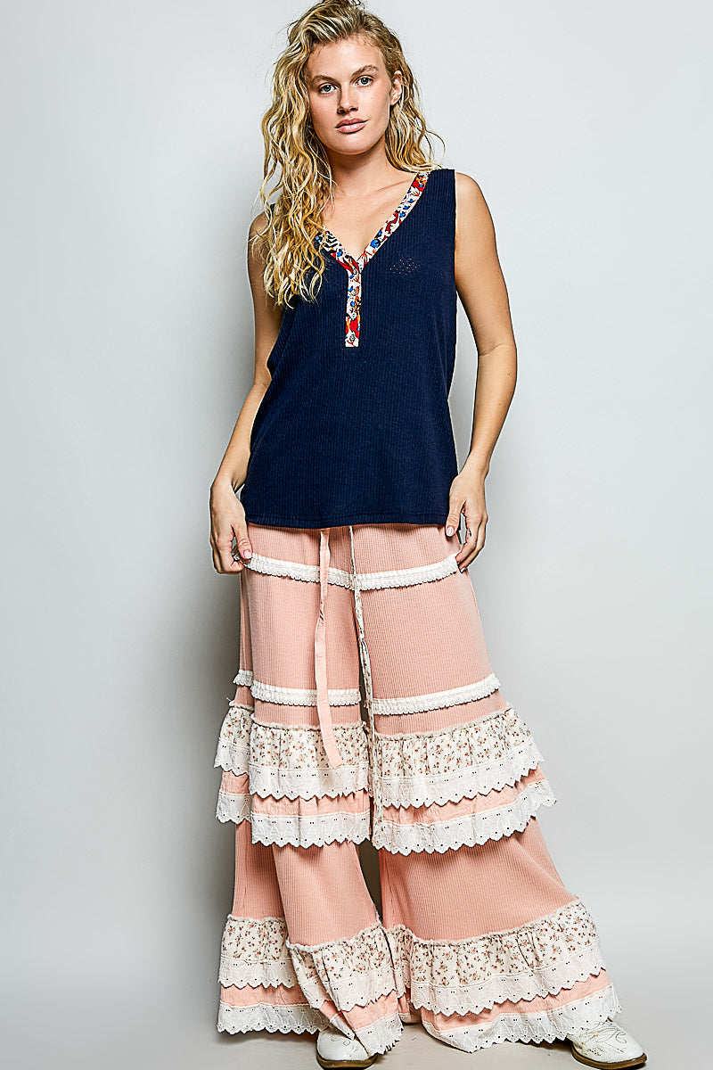 Woman wearing a navy sleeveless top and pink lace pants on a gray background