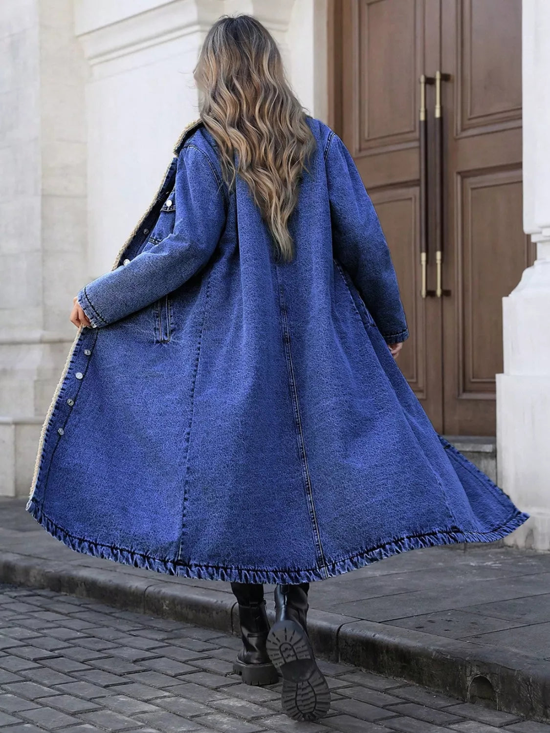 Person wearing a long blue coat walking on a street.