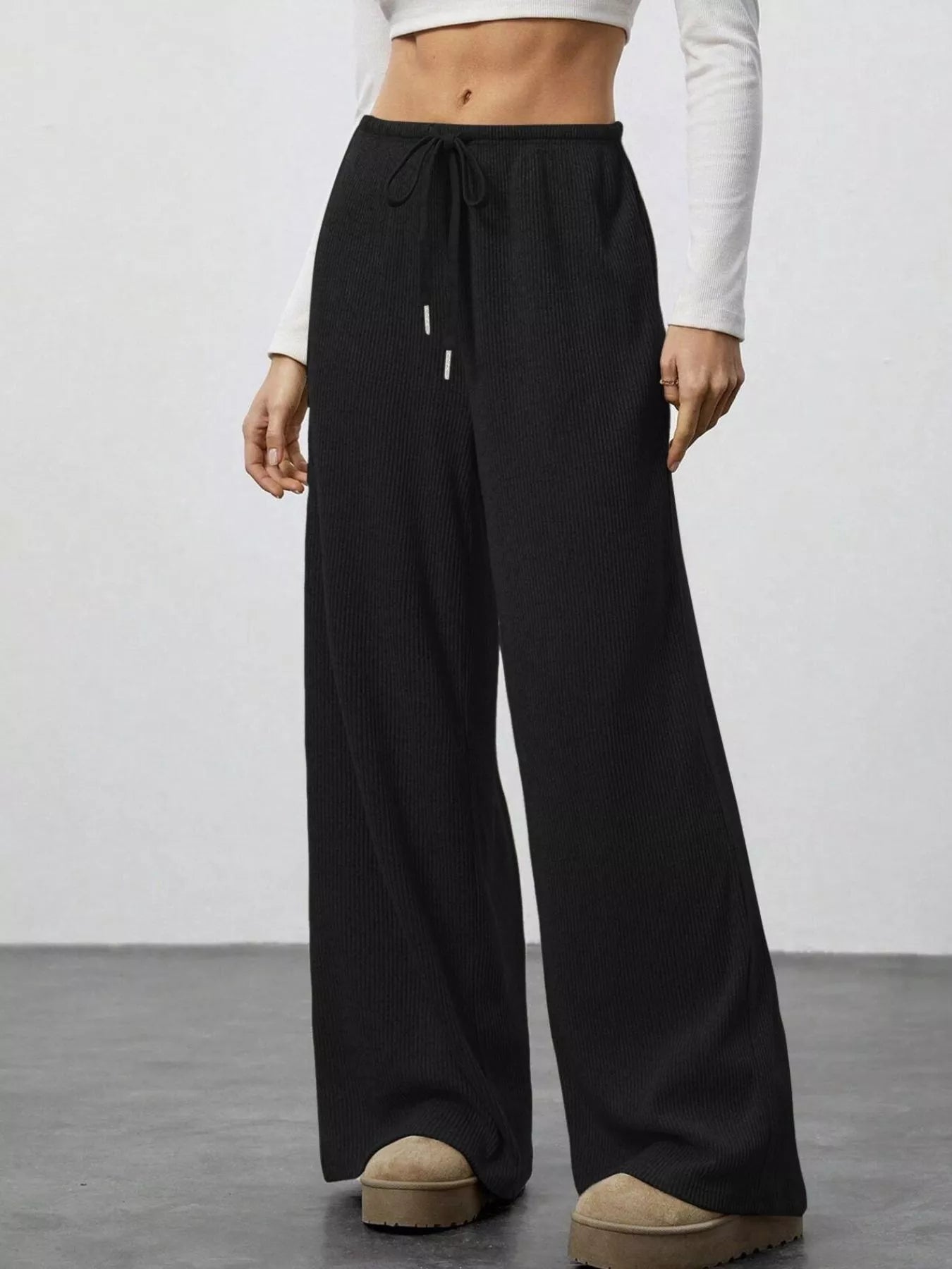 Person wearing black wide-leg pants with a white top on a plain background
