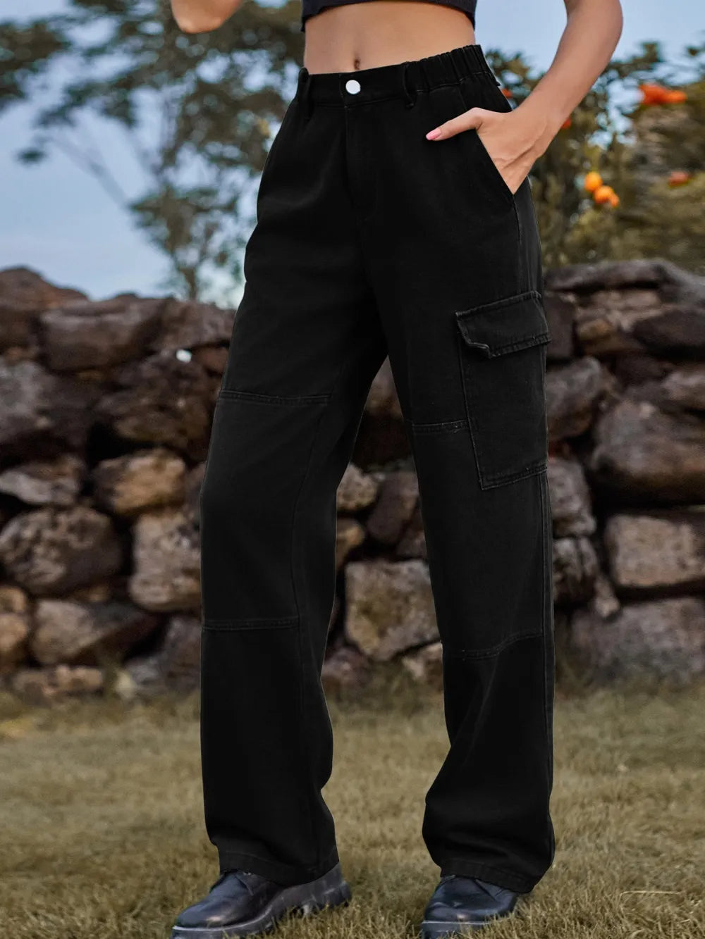 Person wearing black cargo pants standing in front of a stone wall.