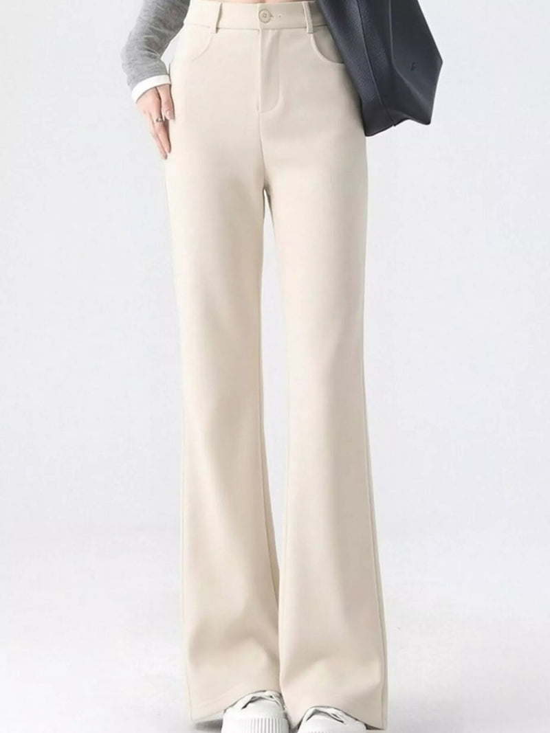A person wearing high-waisted, wide-leg cream pants with a gray long-sleeve top, a dark blazer, and white sneakers, shown from the waist down against a light gray studio background.