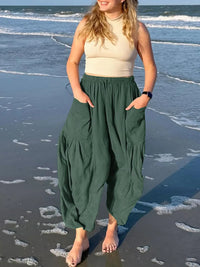 Woman wearing a beige top and green harem pants on a beach.