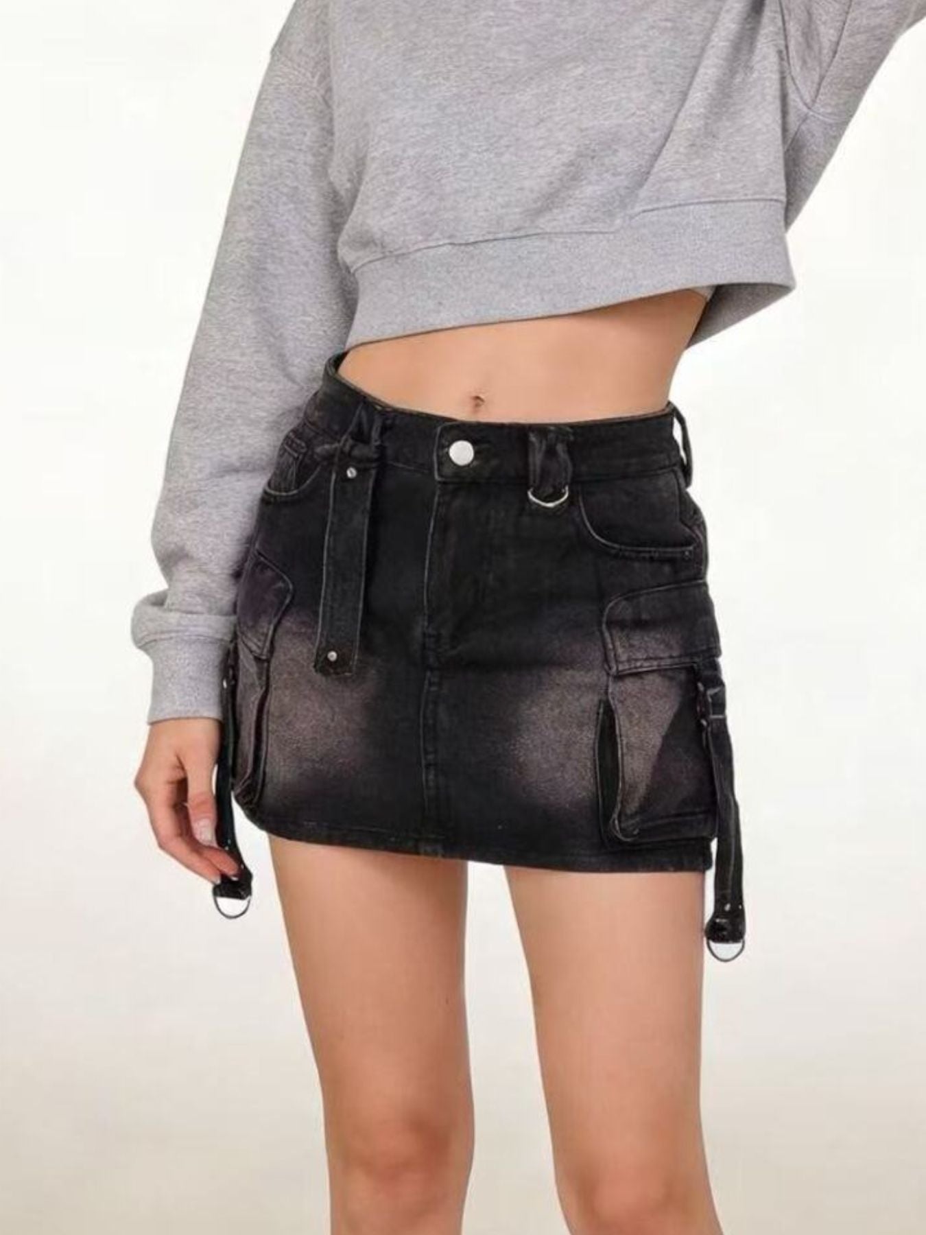 Person wearing a black denim skirt with suspenders on a plain background