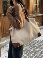 Person holding a beige tote bag with brown accents in front of a wooden door.
