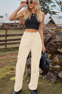 Woman in black crop top and beige cargo pants standing outdoors near a stone wall.
