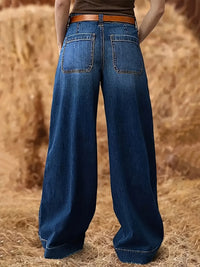 Person wearing blue wide-leg jeans standing in a field of hay.