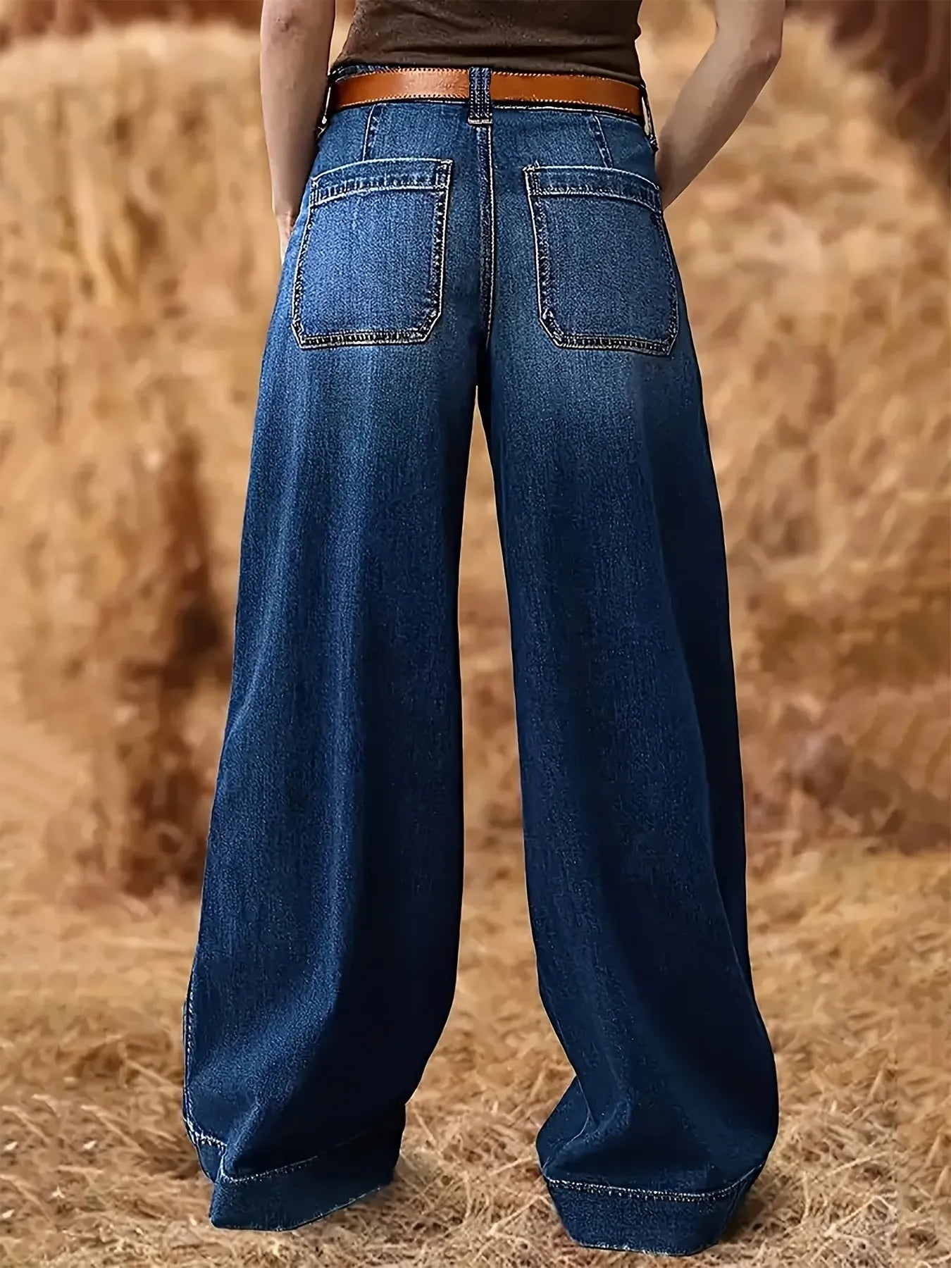 Person wearing blue wide-leg jeans standing in a field of hay.