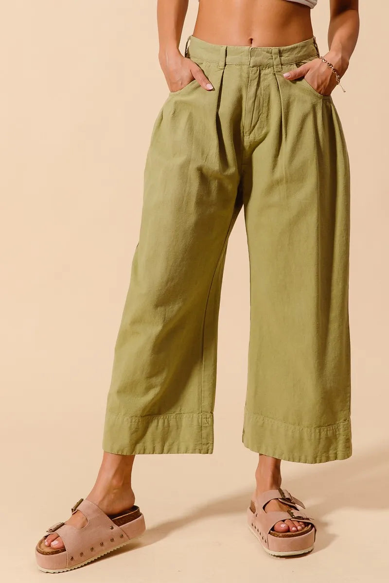 Person wearing green wide-leg pants and sandals on a beige background
