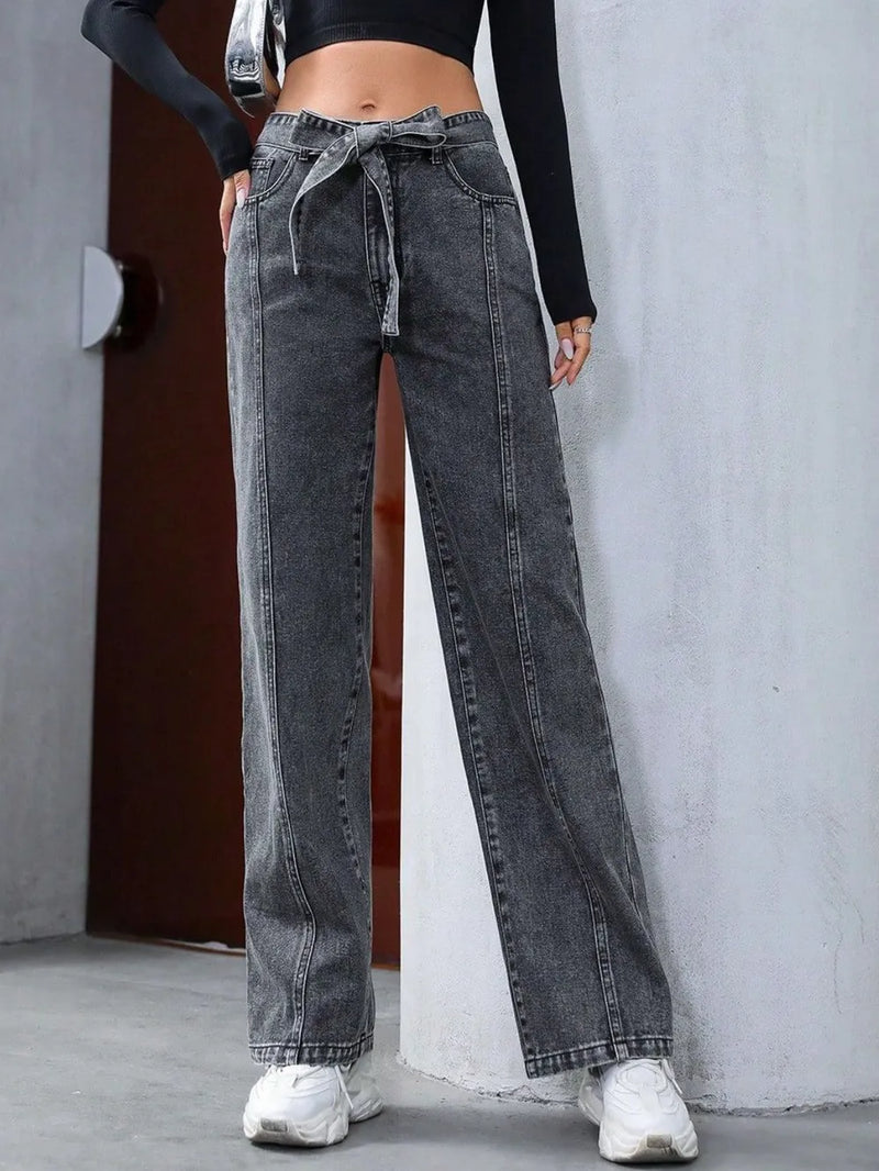 Person wearing high-waisted black jeans with a tie detail on a plain background