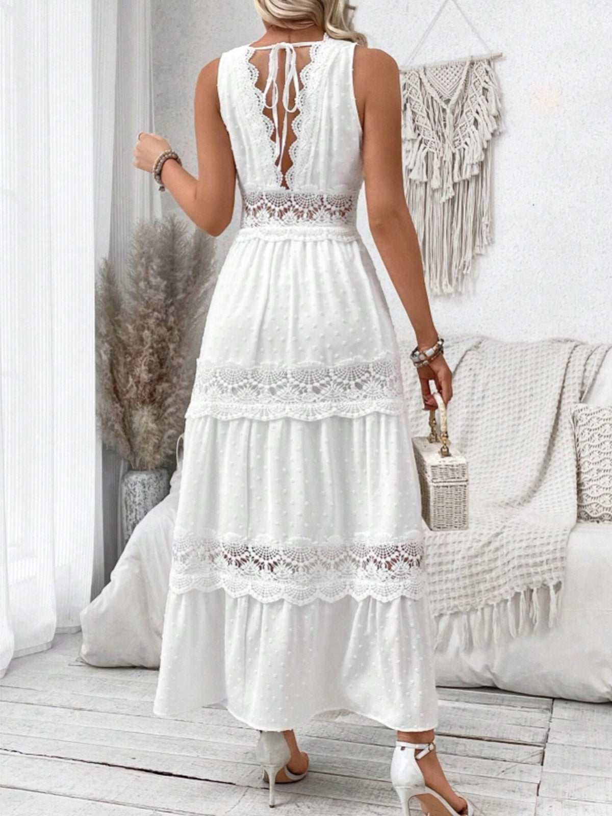 Woman wearing a white lace dress in a bright room with a couch and decorative items.