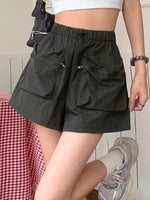 Person wearing dark green shorts with multiple pockets, standing against a light-colored wall.
