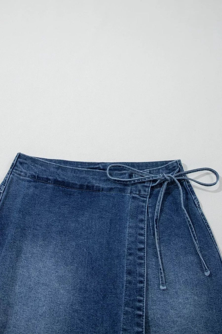 Blue denim skirt with a tie waist on a light gray background