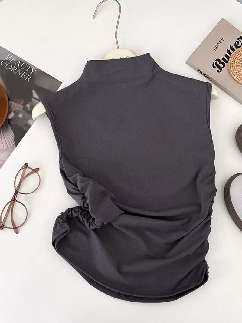 Dark gray sleeveless top on a white surface with books and glasses.