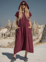 Woman wearing a burgundy dress with a hood in a desert landscape with rock formations.