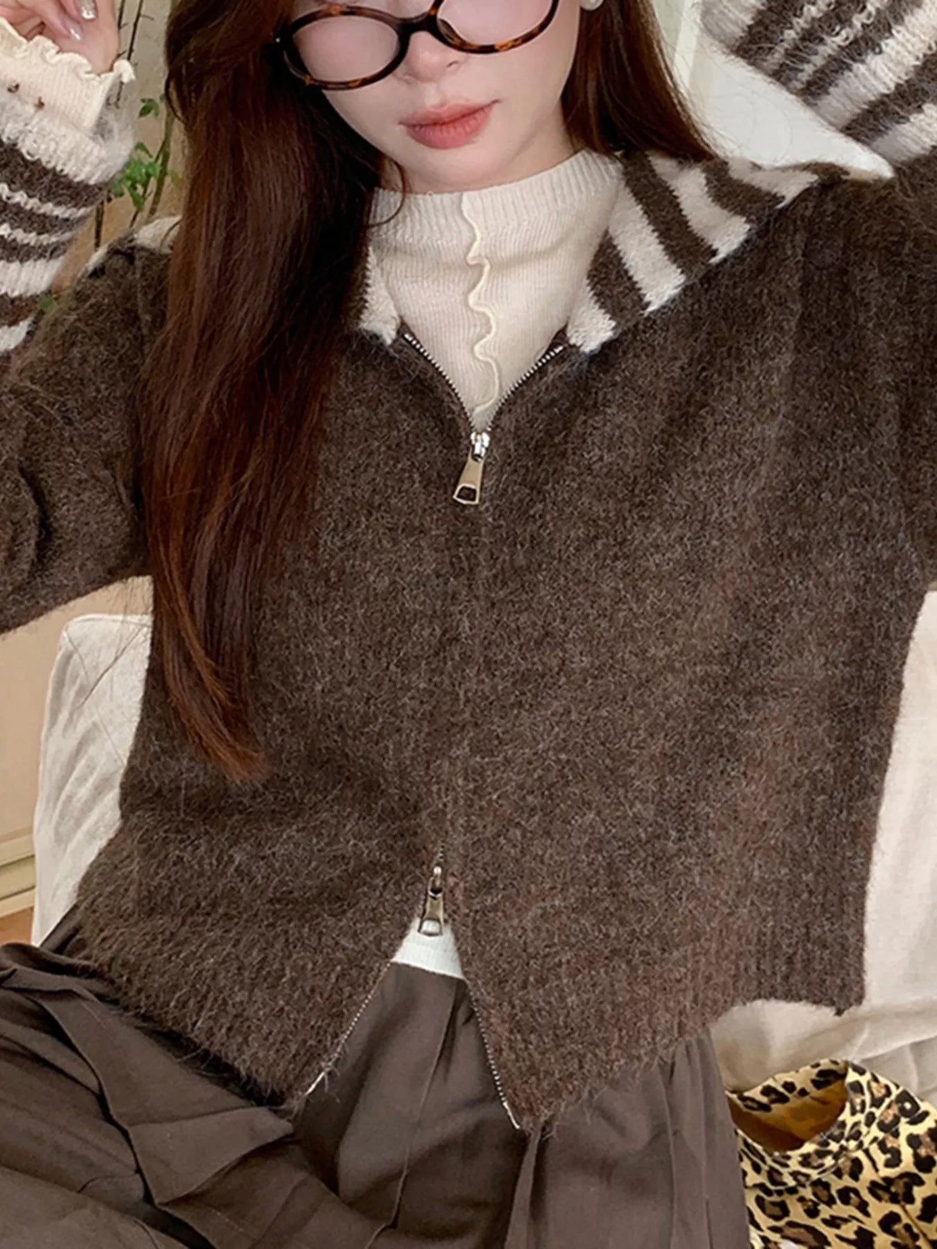 Person wearing a brown zip-up sweater over a white shirt, with a zebra-patterned hat on.