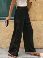 Person wearing black wide-leg pants with star patterns against a beige wall.