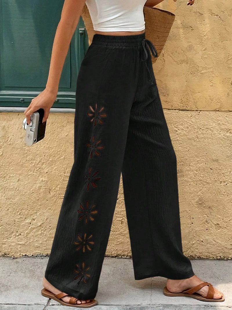 Person wearing black wide-leg pants with star patterns against a beige wall.