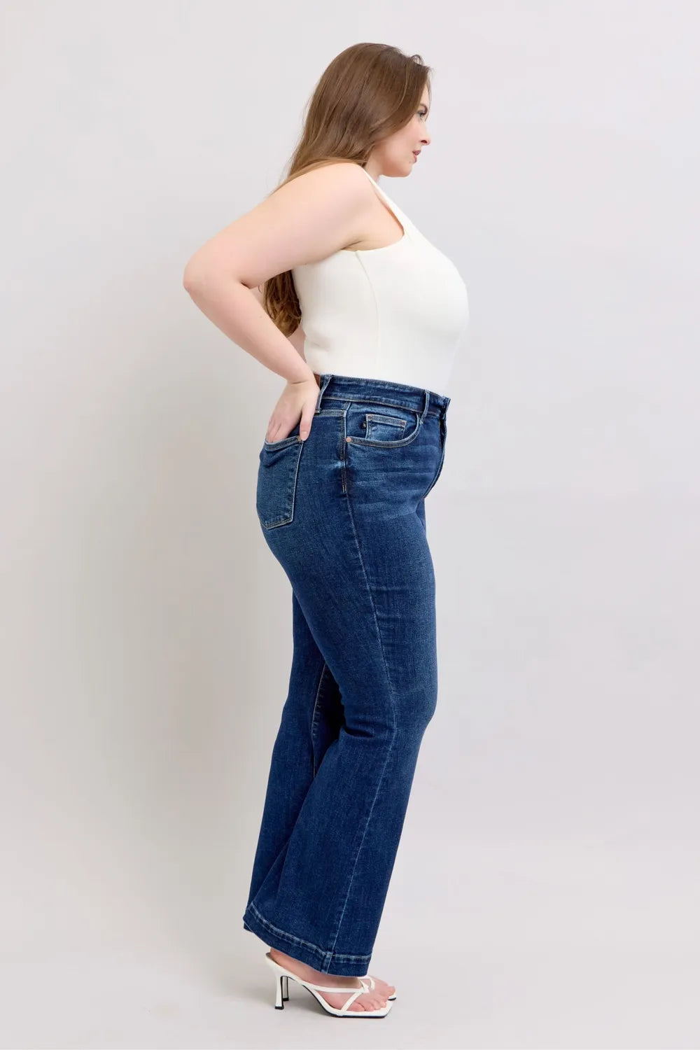 Woman wearing blue jeans and a white top on a plain background