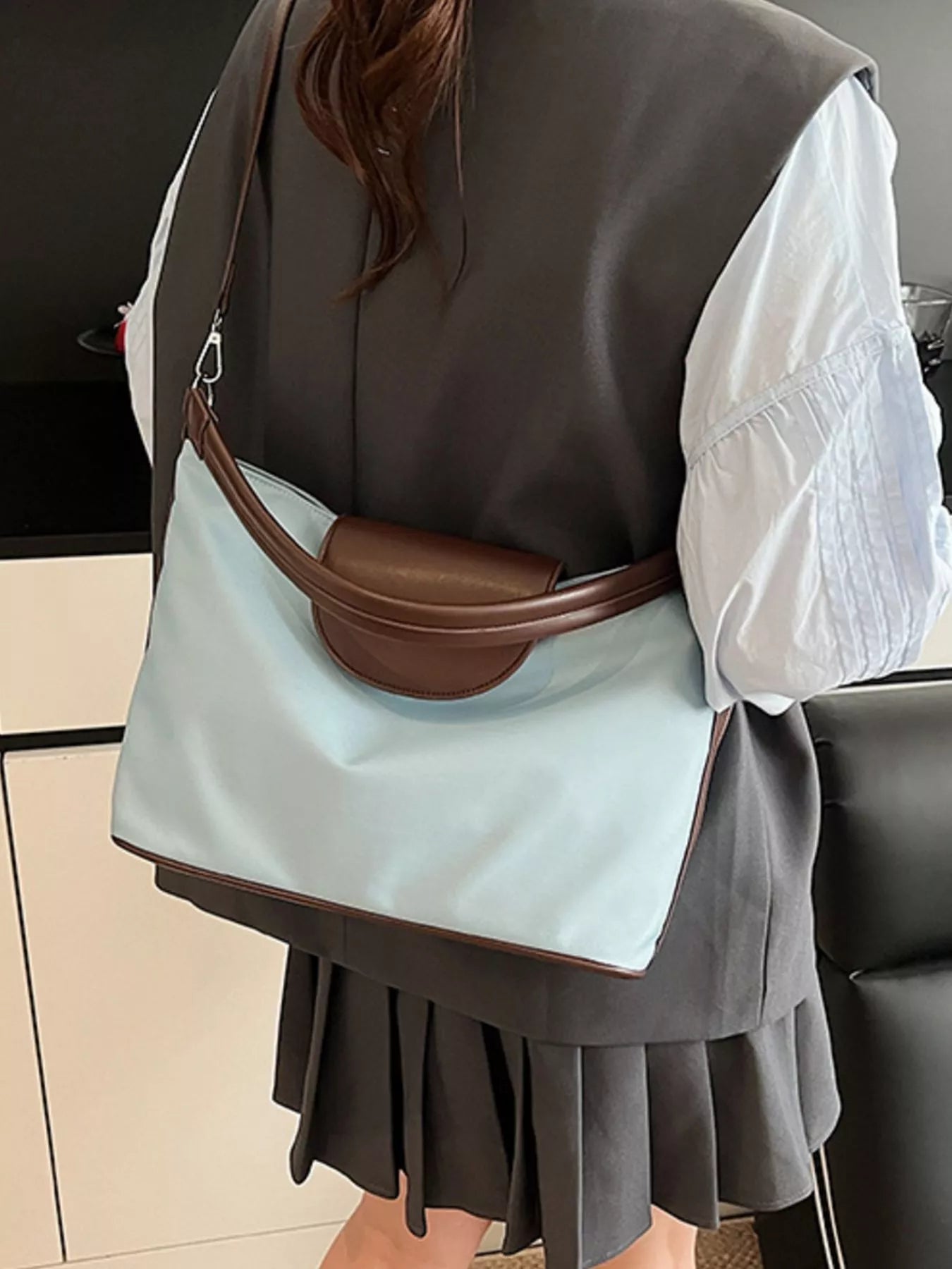 Person wearing a light blue bag with brown accents over their shoulder.
