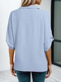 Person wearing a light blue textured shirt with rolled-up sleeves.
