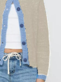 Person wearing a blue cardigan with button details, white shirt, and denim jeans.