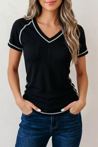 Woman wearing a black ribbed top with white trim and blue jeans on a plain background