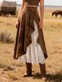 Person wearing a brown and white dress in a desert landscape with a horse and wagon in the background.