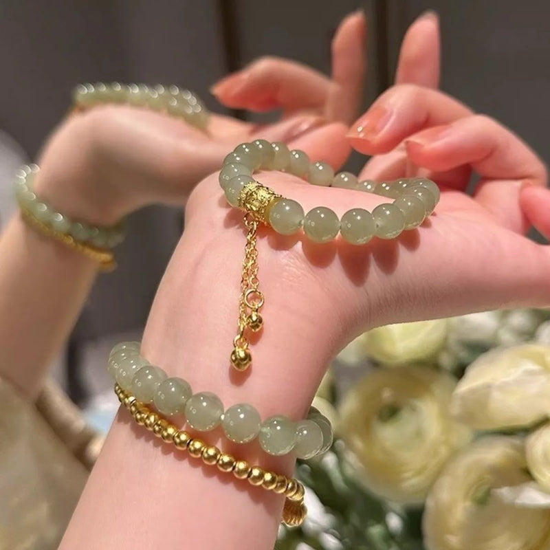 Close-up of hands wearing green beaded bracelets with gold chains against a blurred floral background
