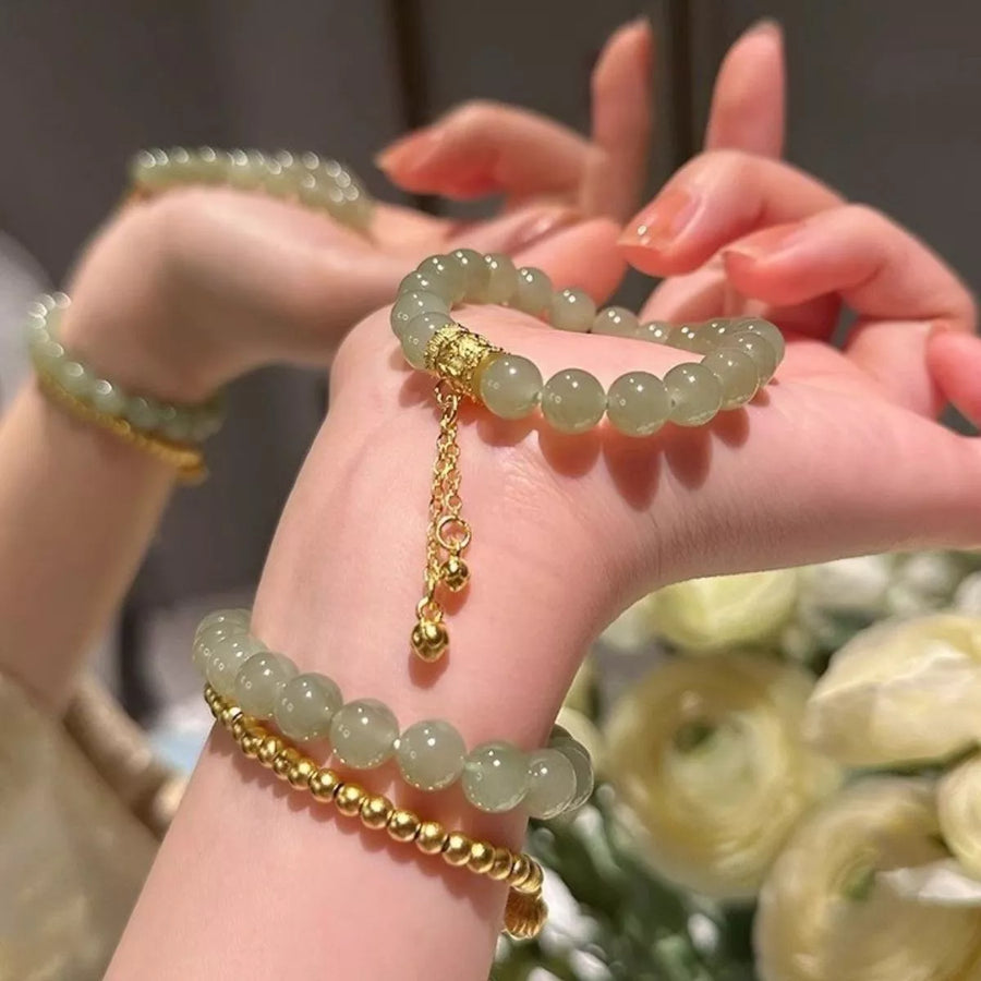 Close-up of hands wearing green beaded bracelets with gold chains against a blurred floral background