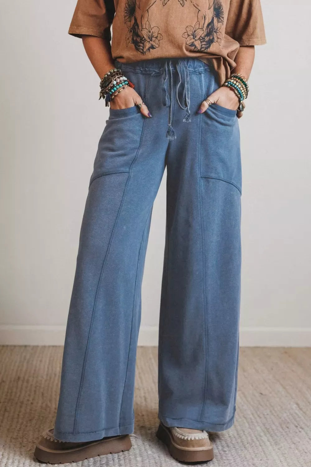 Person wearing blue wide-leg jeans and a brown shirt with a tattoo design, standing against a plain background.