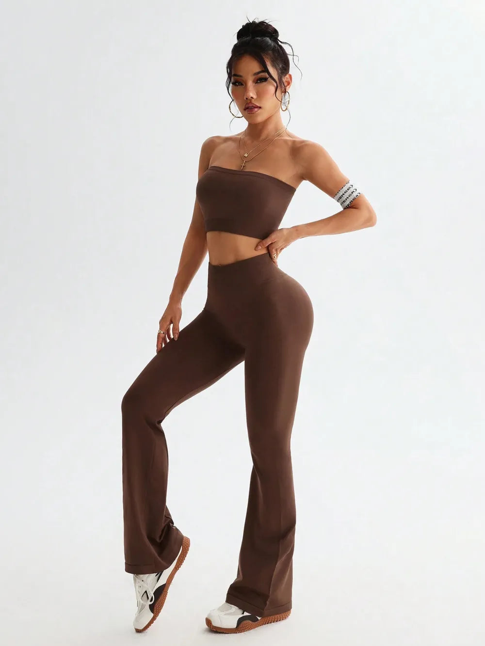 Woman wearing a brown strapless top and flared pants on a white background