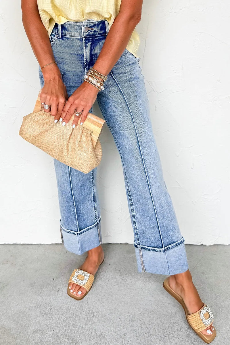 Person wearing blue jeans and yellow top holding a beige clutch against a white background