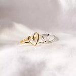 Two heart-shaped rings, one gold and one silver, on a light fabric background.