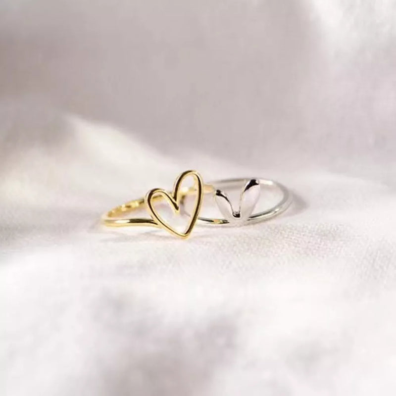 Two heart-shaped rings, one gold and one silver, on a light fabric background.