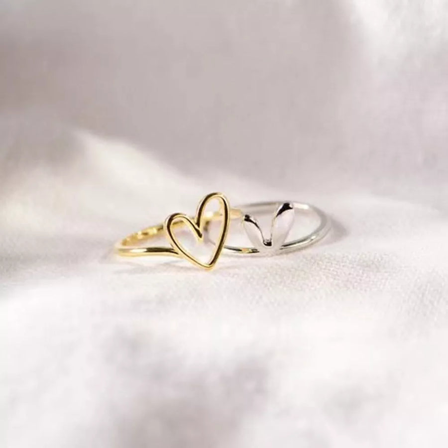 Two heart-shaped rings, one gold and one silver, on a light fabric background.